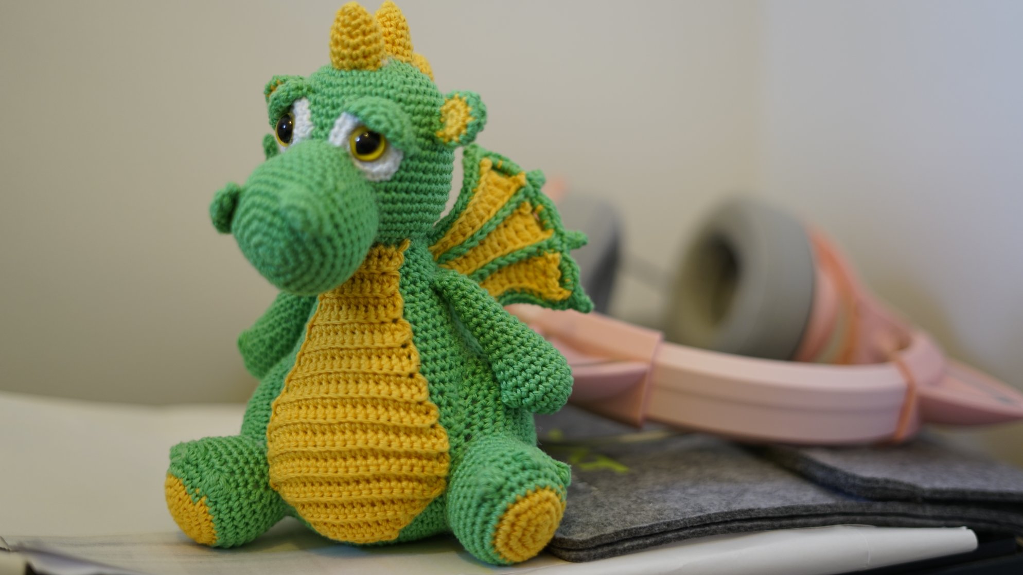 Grüner Häkelndrache, vor rosa Kopfhörern