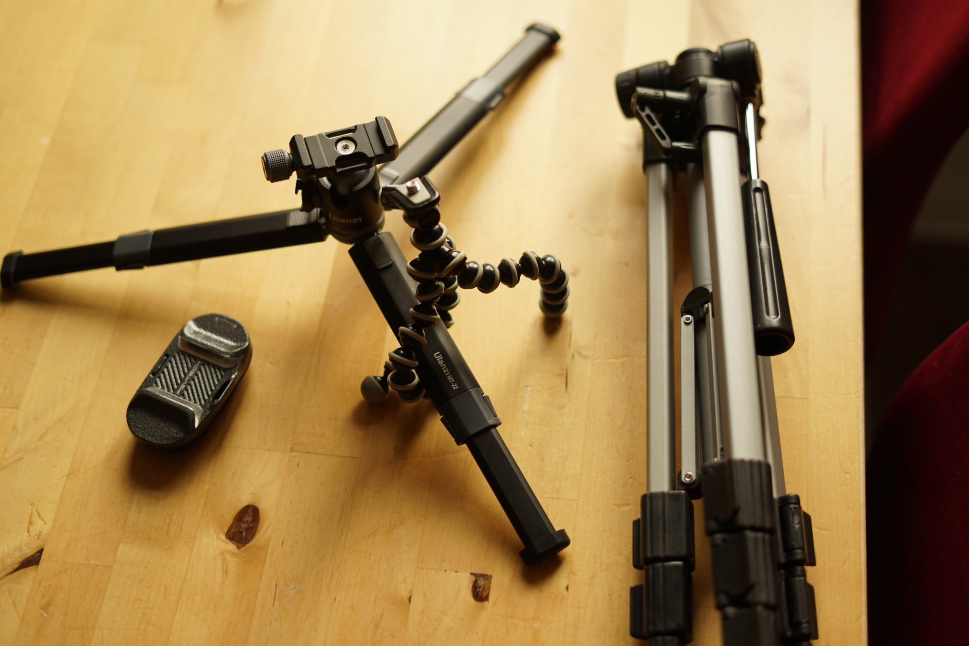 Die Stative auf dem Tisch
Das mittelgroße in seiner maximalen Breite ausgeklappt, das Gorillapod-Ding darum gewickelt.

Der Bildrahmen reicht nicht aus um das große Stativ auszuklappen - also zusammengeklappt.

Daneben noch eine Halterung um die Kamera an den Rucksack-Träger zu hängen.