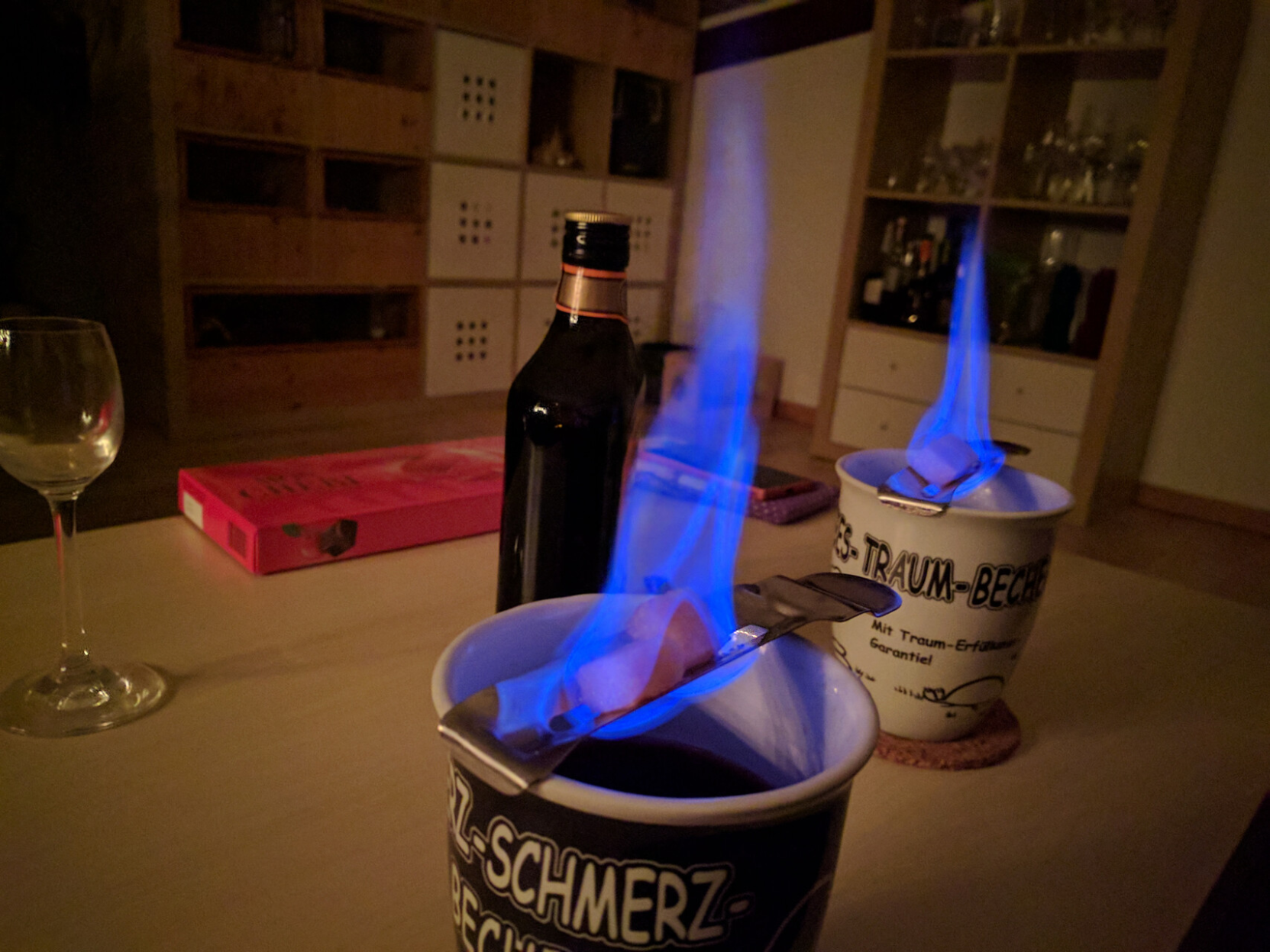 Zwei billige Steingut-Tassen, auf jeder liegt ein Absinth-Löffel mit blau brennenden Zuckerstückchen
Davor eine Flasche Stroh80 Zwei billige Steingut-Tassen, auf jeder liegt ein Absinth-Löffel mit blau brennenden Zuckerstückchen
Davor eine Flasche Stroh80