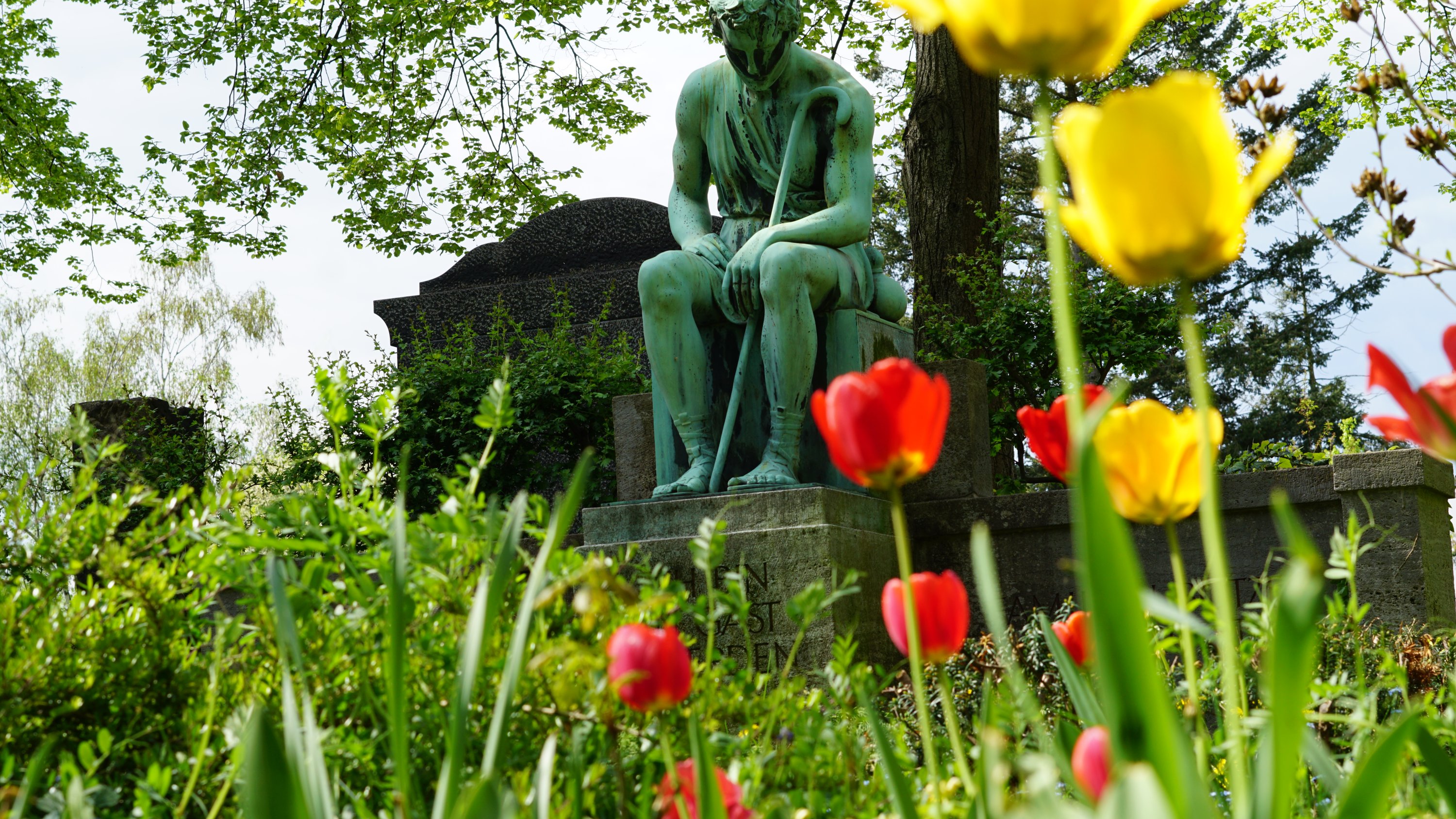 Fokus auf Statue, rote und gelbe Tulpen im Vordergrund 