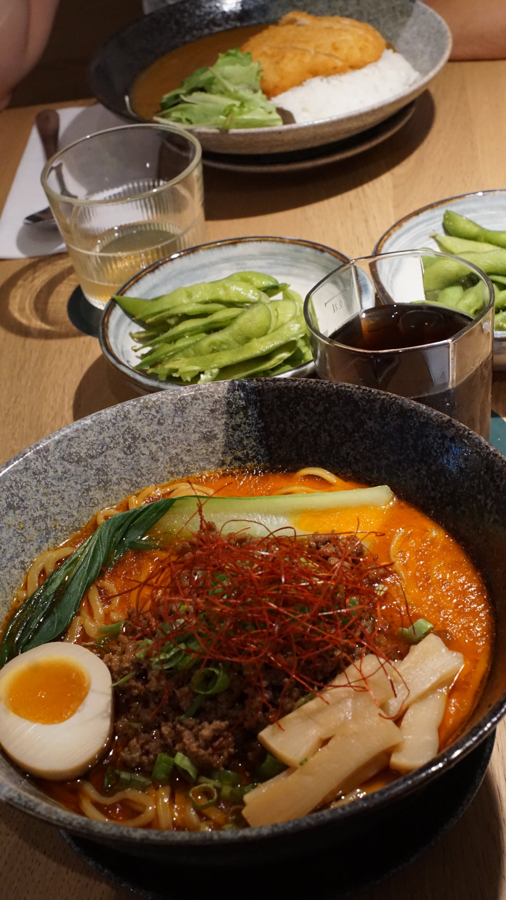Zwei Schüsseln mit japanische, essen. Jeweils Suppe mit sehr viel Einlagen. Die Schüssel im Vordergrund enthält unter anderem ein halbes ei, rote Brühe, Nudeln, Gemüse und Chili-Fäden.

Es wirkt (zu recht) eher relativ scharf.

In der Mitte des Tisches stehen Sojabohnen mit Salz als Vorspeise.