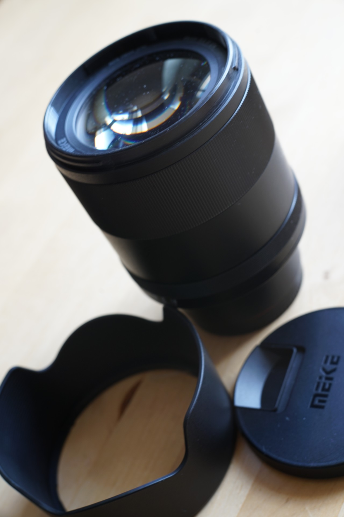 Das Objektiv neben seinem Deckel und der Streulichtblende - es hat eine unglaublich großformatige Glasfront