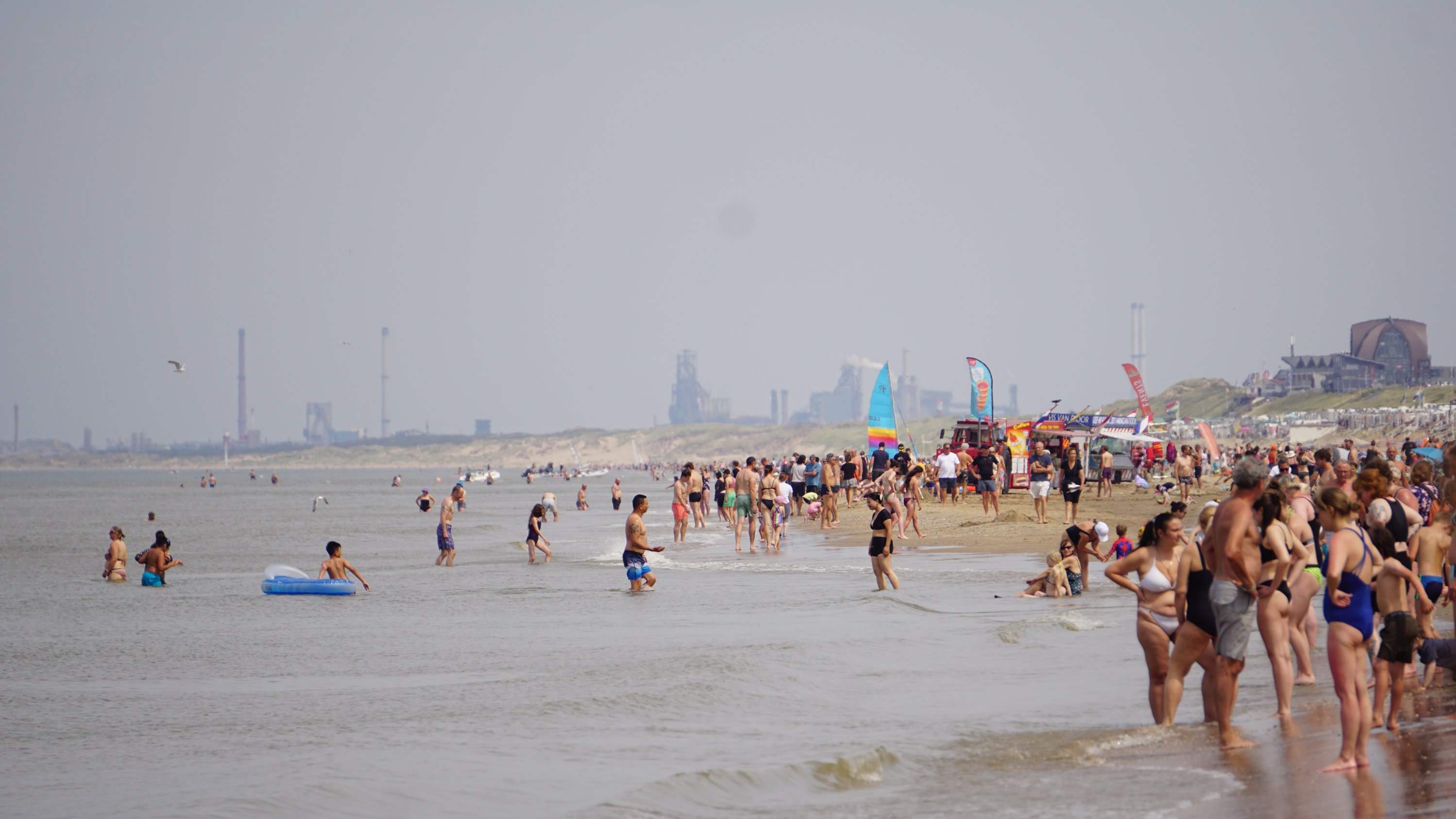 Langer Blick am Ufer entlang - mehr Menschen als Sand 
Am Ende industrialisierte Bauten