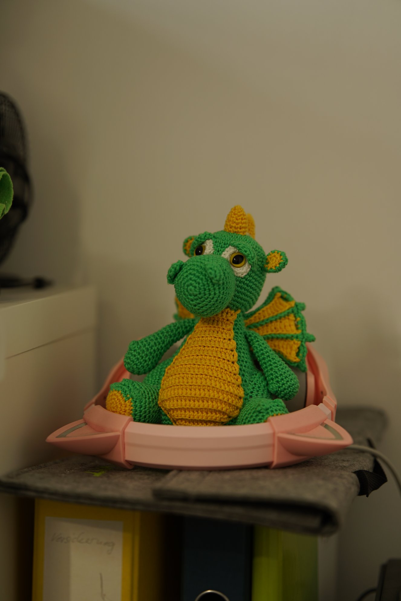 Ein grün-gelber Häkeldrache umgeben von rosa Kopfhörern mit Ohren 