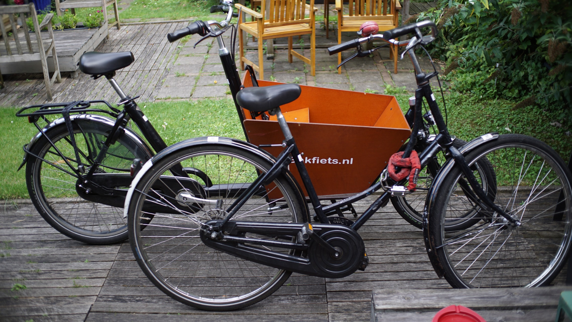 Zwei ausgeliehene Fahrräder in einem Garten. Ein klassisches Hollandrad, ein Bakfiets-Lastenrad. Beide mit bestenfalls suspektem Wartungszustand.