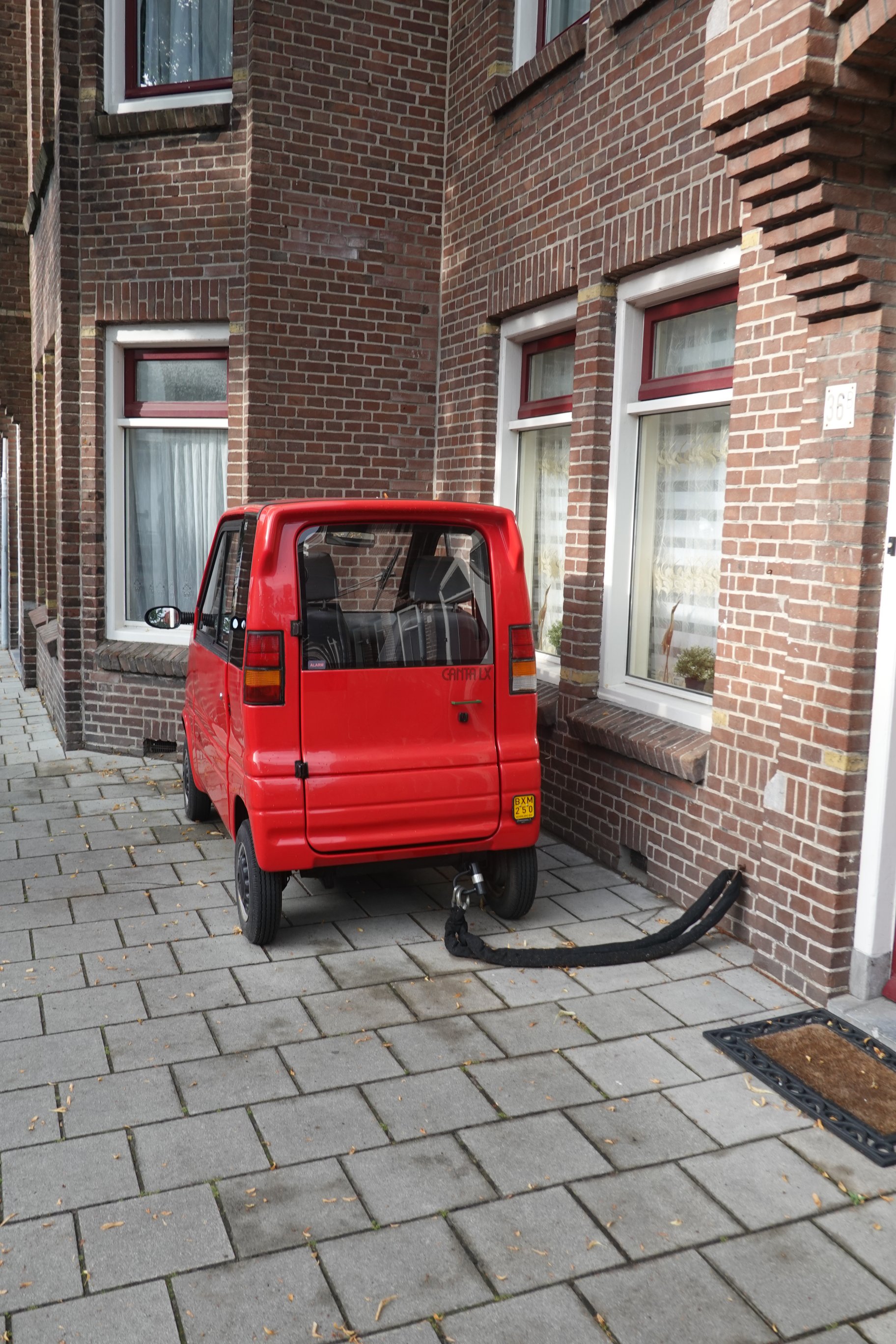 Kleines, rotes Fahrzeug, mit einer schweren Kette am Haus befestigt.