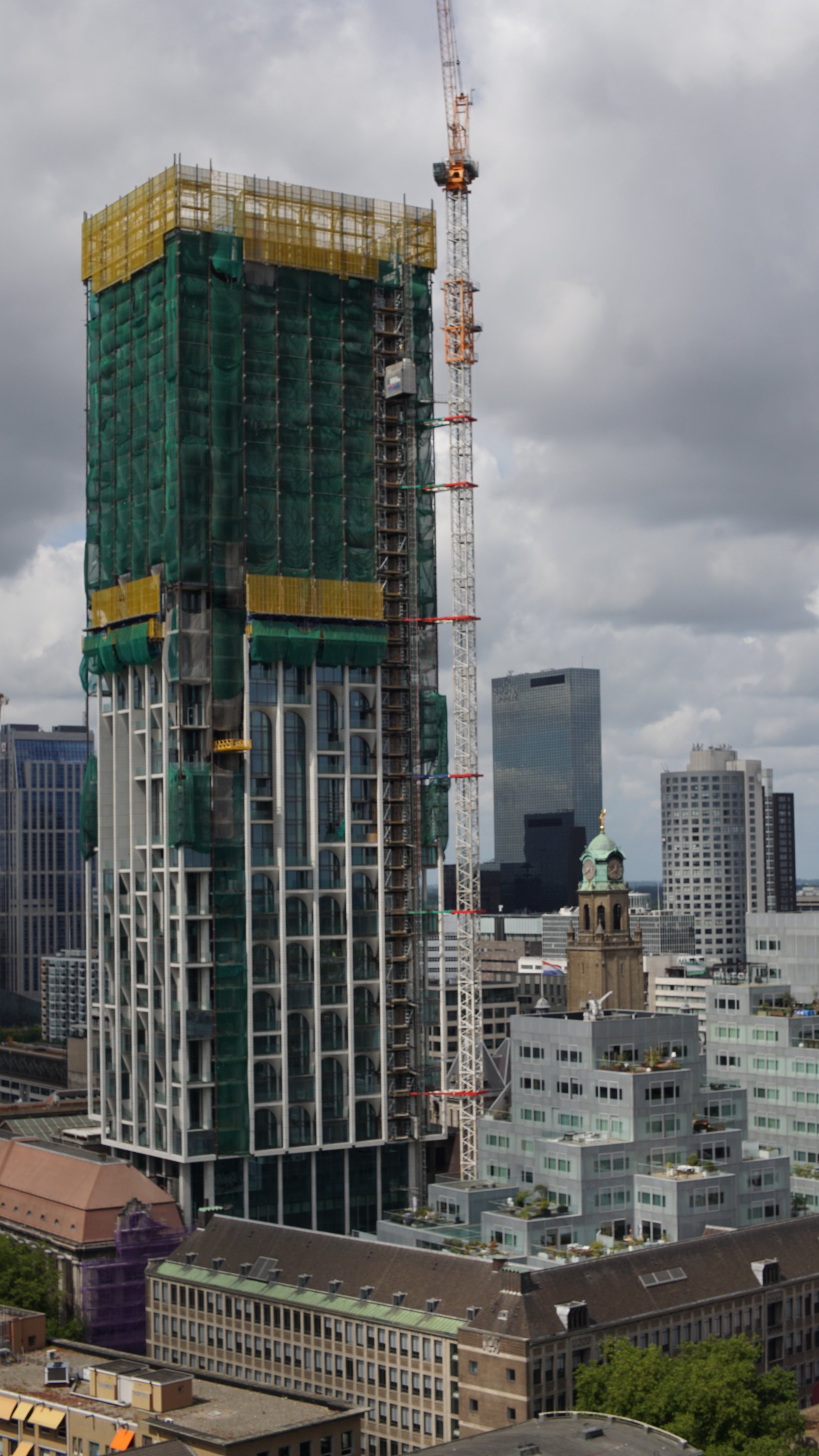 Hochhaus mit markanten Balkon-Strukturen, direkt in den Innenhof älterer Gebäude gesetzt 

Obere Hälfte noch voll eingerüstet, Kran daneben 