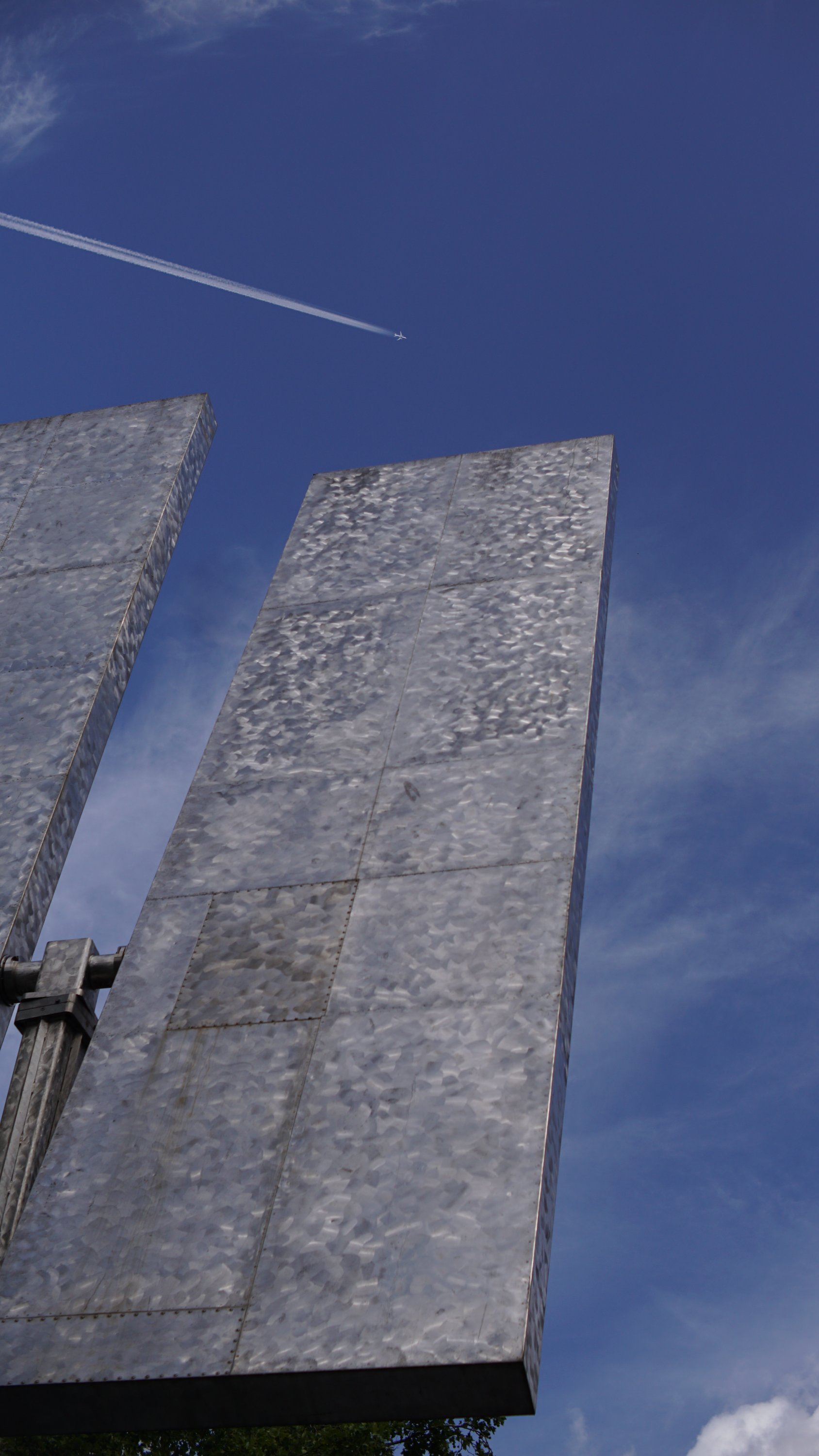 Ca. 2/3 der rechten/oberen Seite des genannten Kunstwerkes, darüber blauer Himmel und Kondensstreifen eines Flugzeuges.

Das Kunstwerk besteht, passend zum Namen, aus zwei länglichen Metallflächen mit glänzender Oberfläche, die um eine gemeinsame Mitte aufgehängt, sich etwa wie Schaufelräder drehen können (nur halt mit jeweils nur zwei Schaufeln)

Die Mitte ist an einer senkrechten Achse aufgestellt, die sich ebenfalls dreht.

Einige Teile der Edelstahl-Oberfläche zeigen trotzdem bereits Rost
