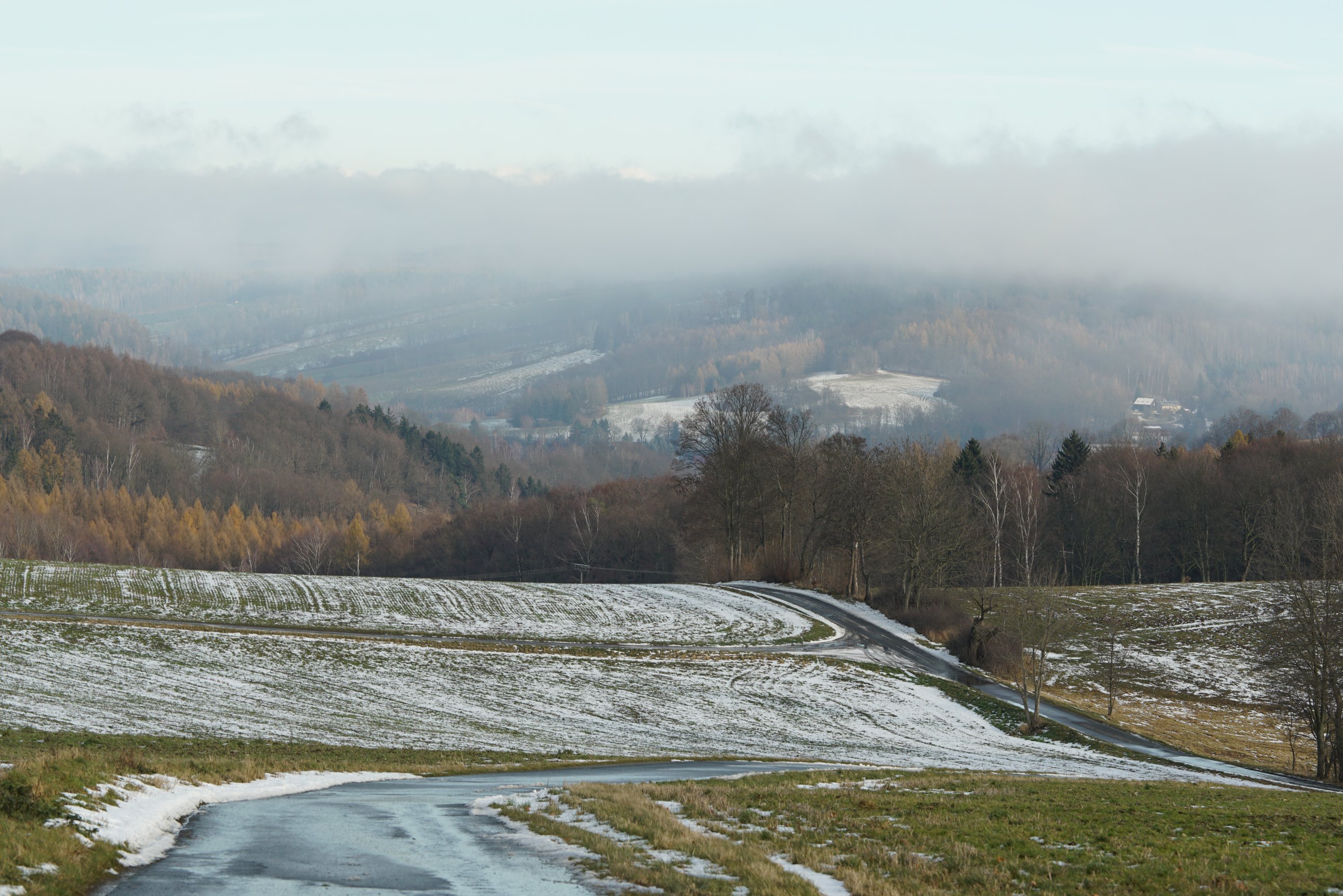Blick ins Tal, Wolken oberhalb dessen, weitere Straße mit mehreren Abzweigungen

Leichte Schneereste auf Feldern 