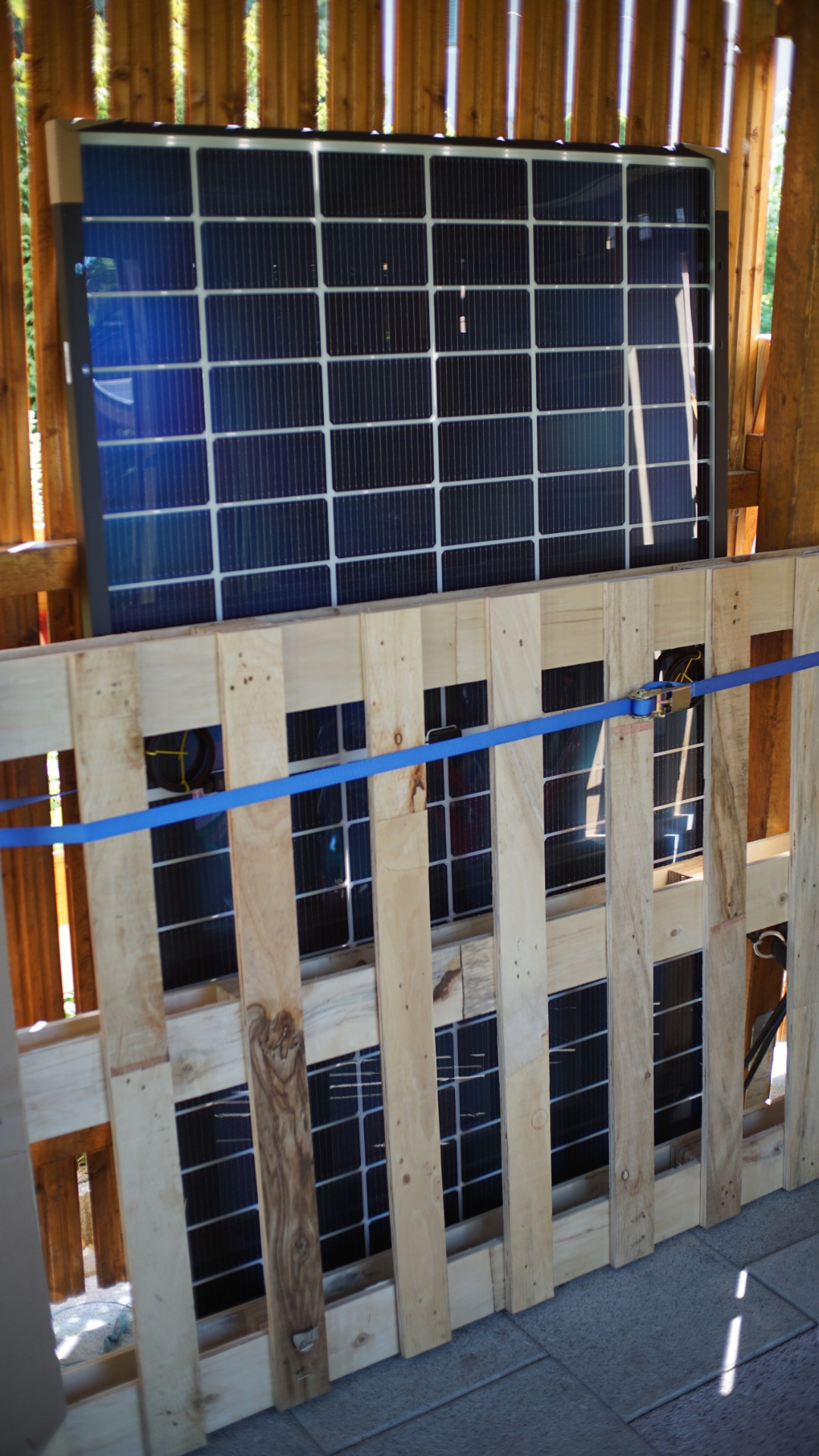 Ein Solarpanel ist an einer Holzwand angebunden (Palette steht davor, Spanngurt um die Palette, damit flächiger Druck auf das Panel) Ein Solarpanel ist an einer Holzwand angebunden (Palette steht davor, Spanngurt um die Palette, damit flächiger Druck auf das Panel)