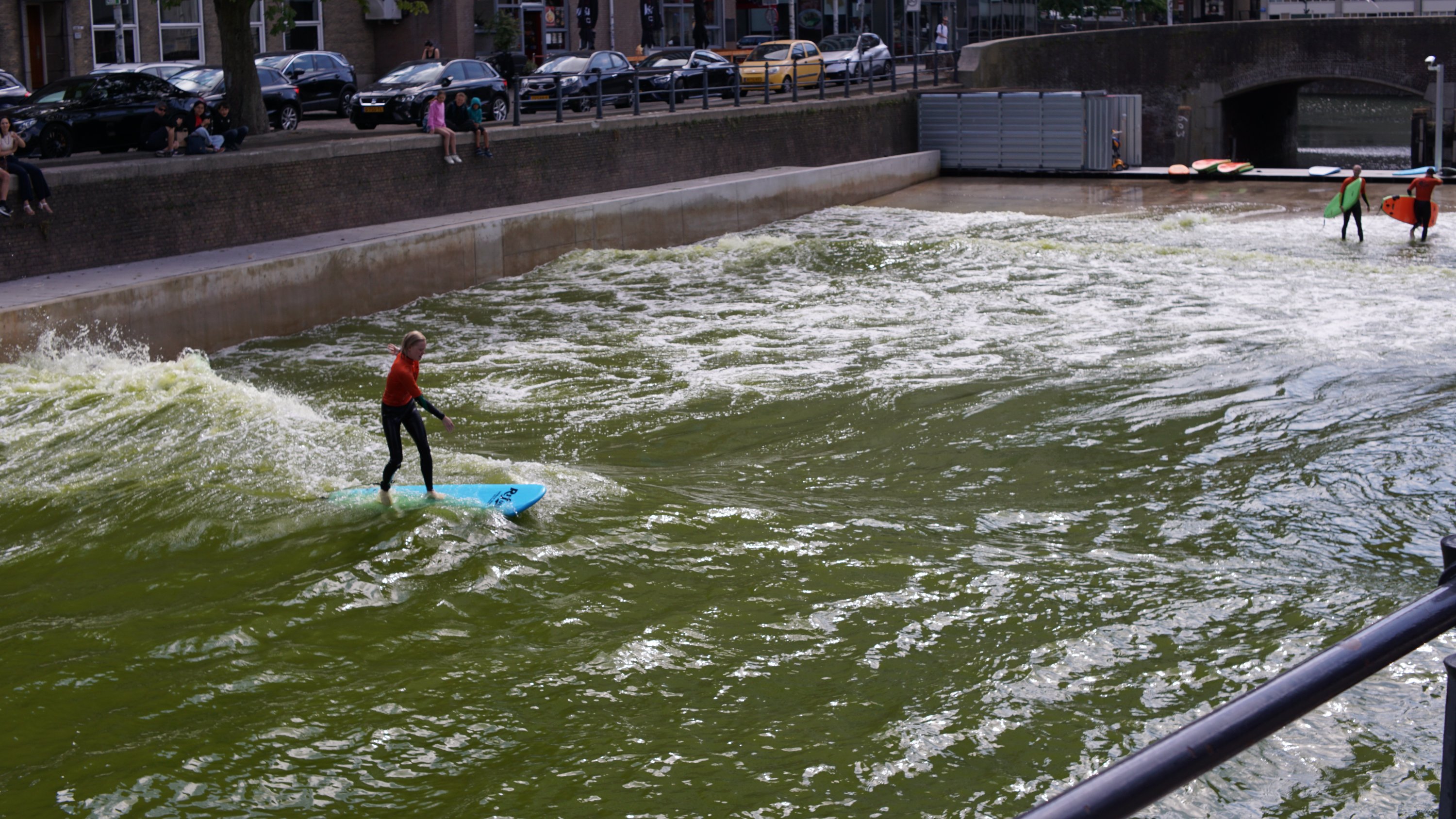 Mehr Umgebung, das Wasser befindet sich in einem Betonloch in der Innenstadt, Autos und Gebäude ringsum 