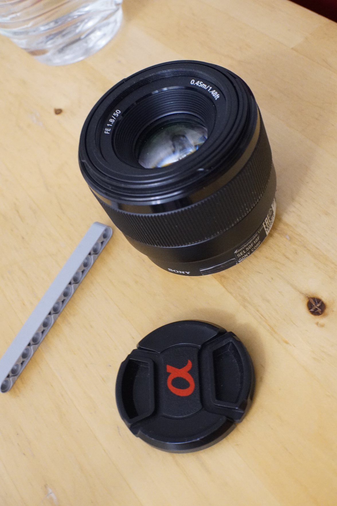 Das Sony-Objektiv mit offenem Deckel, neben einem Klemmbaustein-Technic-Liftarm (for scale)