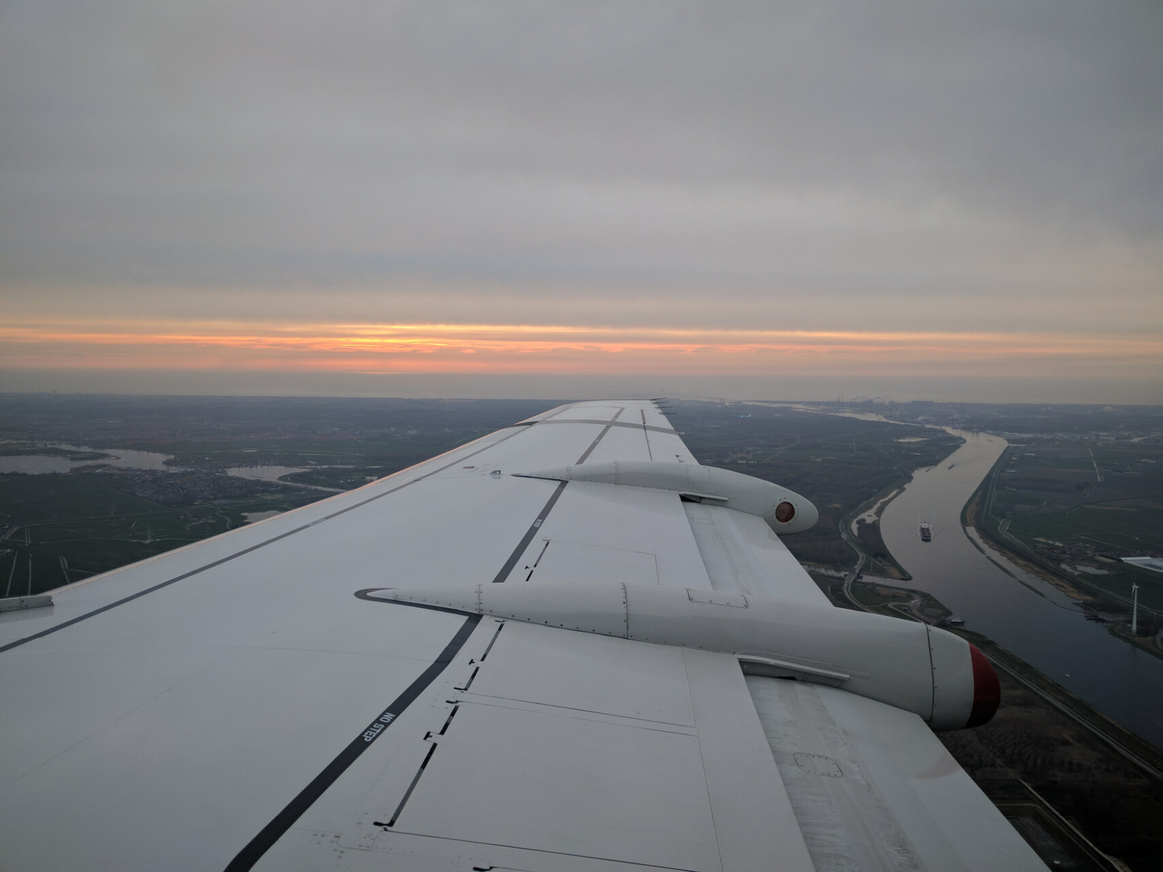 Eine Tragfläche, darunter ein Fluss mit Schiff, Sonnenuntergang am Horizont. Eine Tragfläche, darunter ein Fluss mit Schiff, Sonnenuntergang am Horizont.