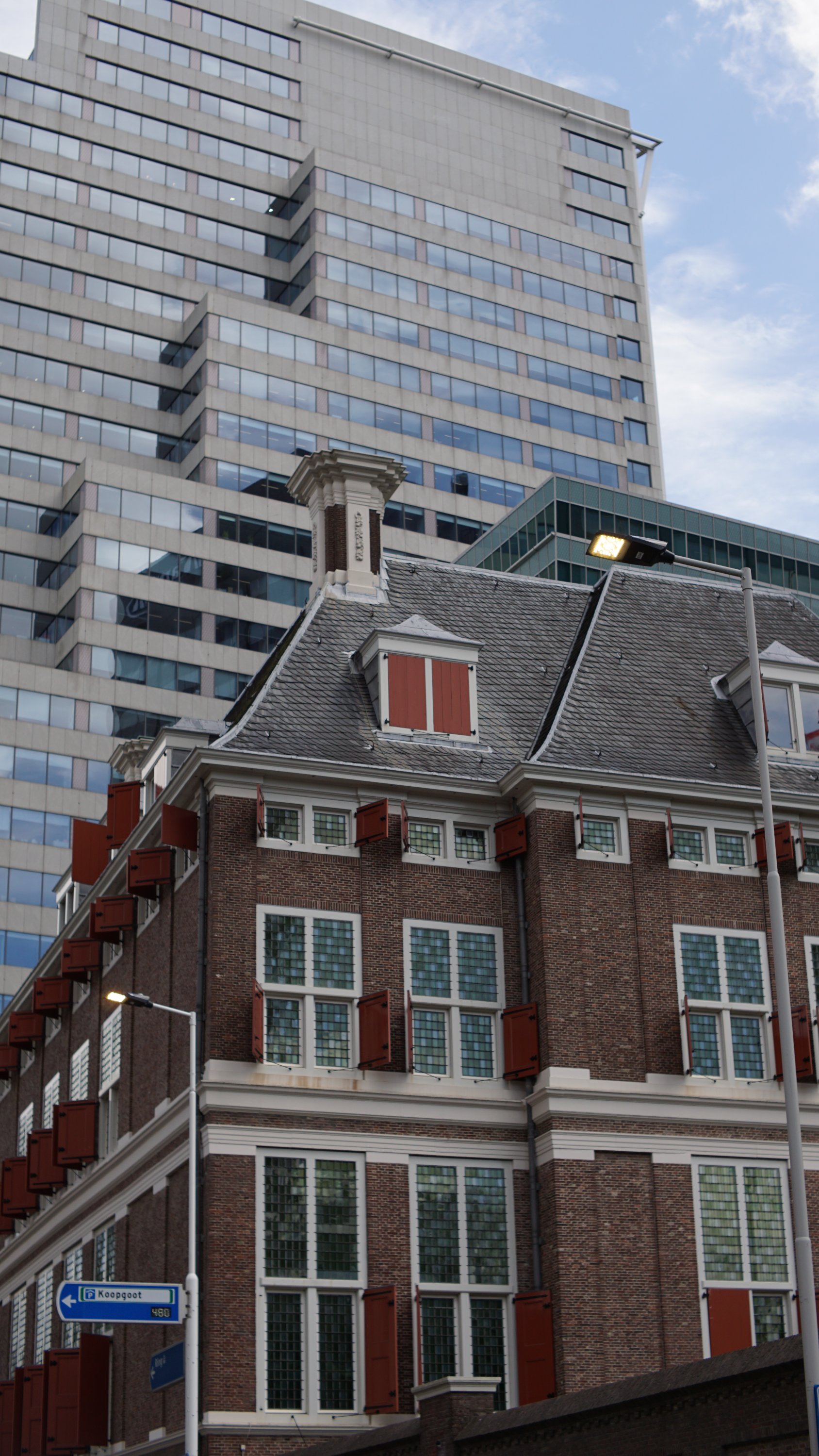 Ein niedrigeres Haus aus roten Ziegeln, dahinter Stahlbeton-Hochhaus 
