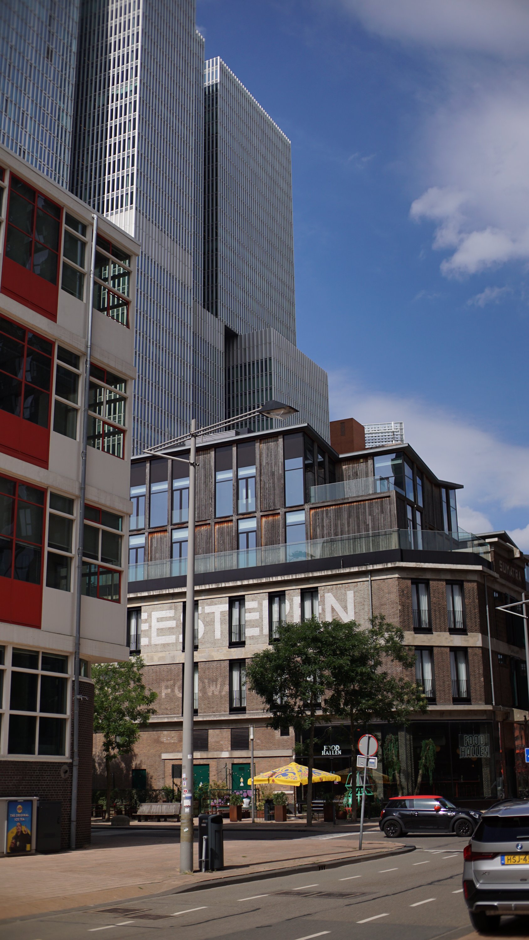 Ca. 5-stöckiges Hallen-Gebäude zwischen Hochhäusern in Rotterdam 
Straße im Vordergrund 
Man kann "Foodhallen" als Schild über einem Eingang erkennen 