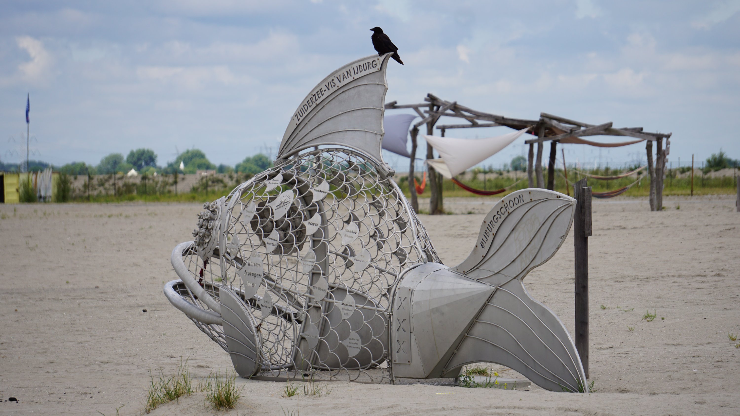 Metallfisch am Strand, ein Rabenvogel sitzt drauf