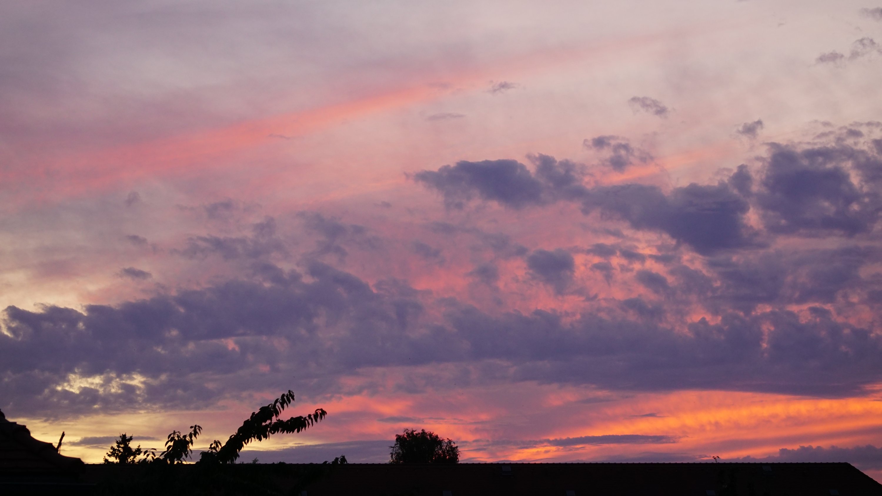 Hausdach, darüber Wolken in unterschiedlichen Farben 