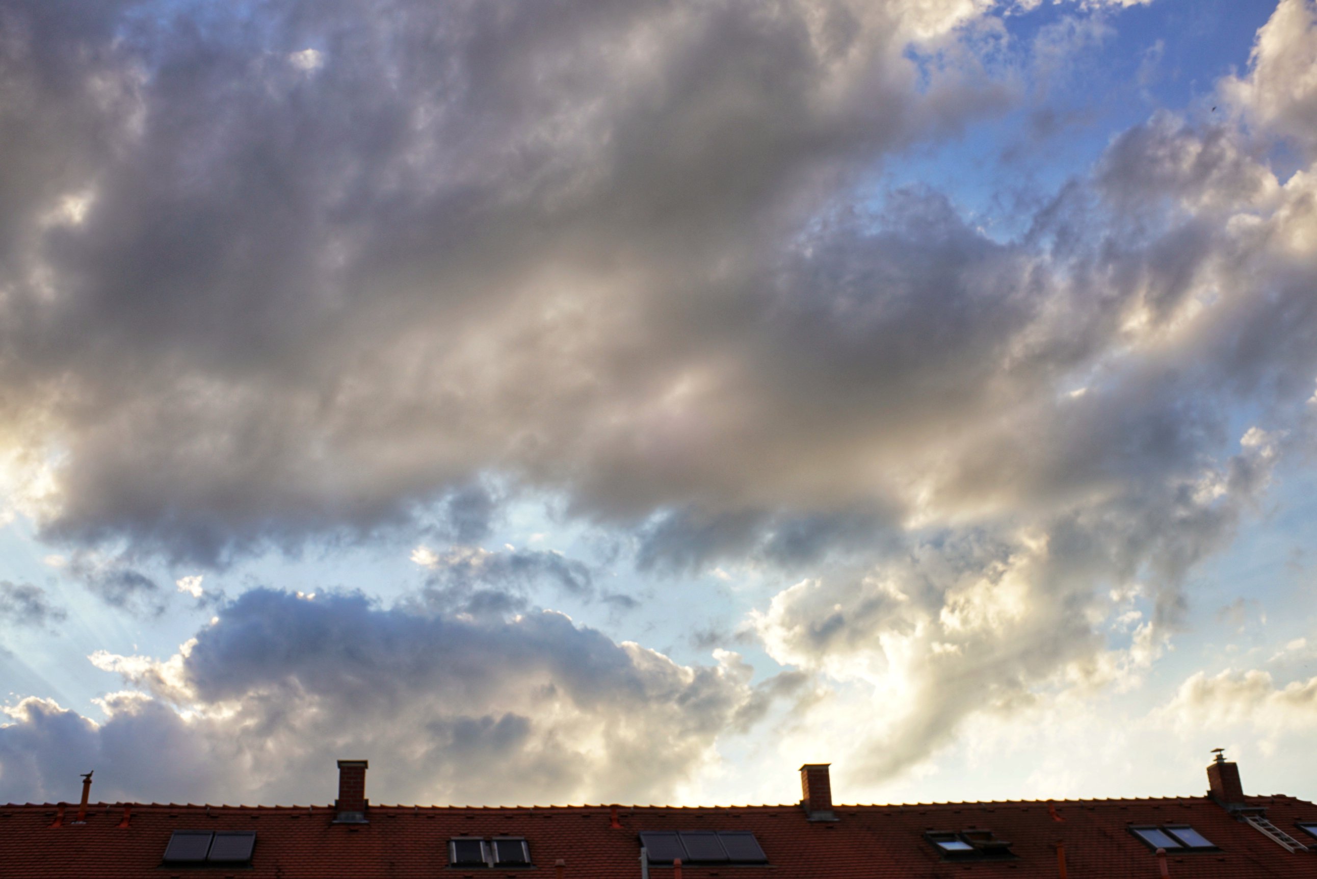 Wolken über einem Dach gold/grau mit blauem Himmel dazwischen 