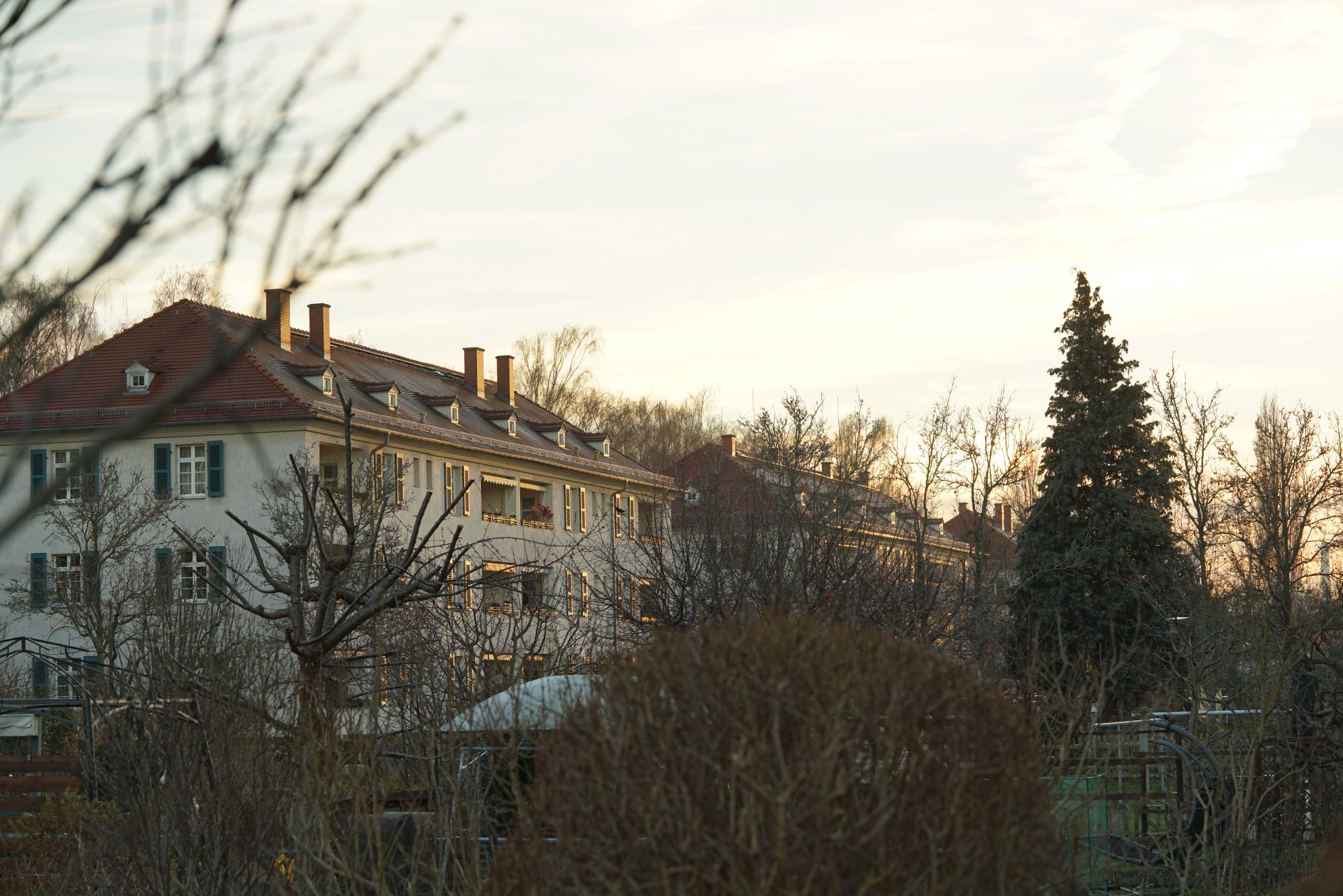 Zwei angeleuchtete Häuser, davor Kleingärten 