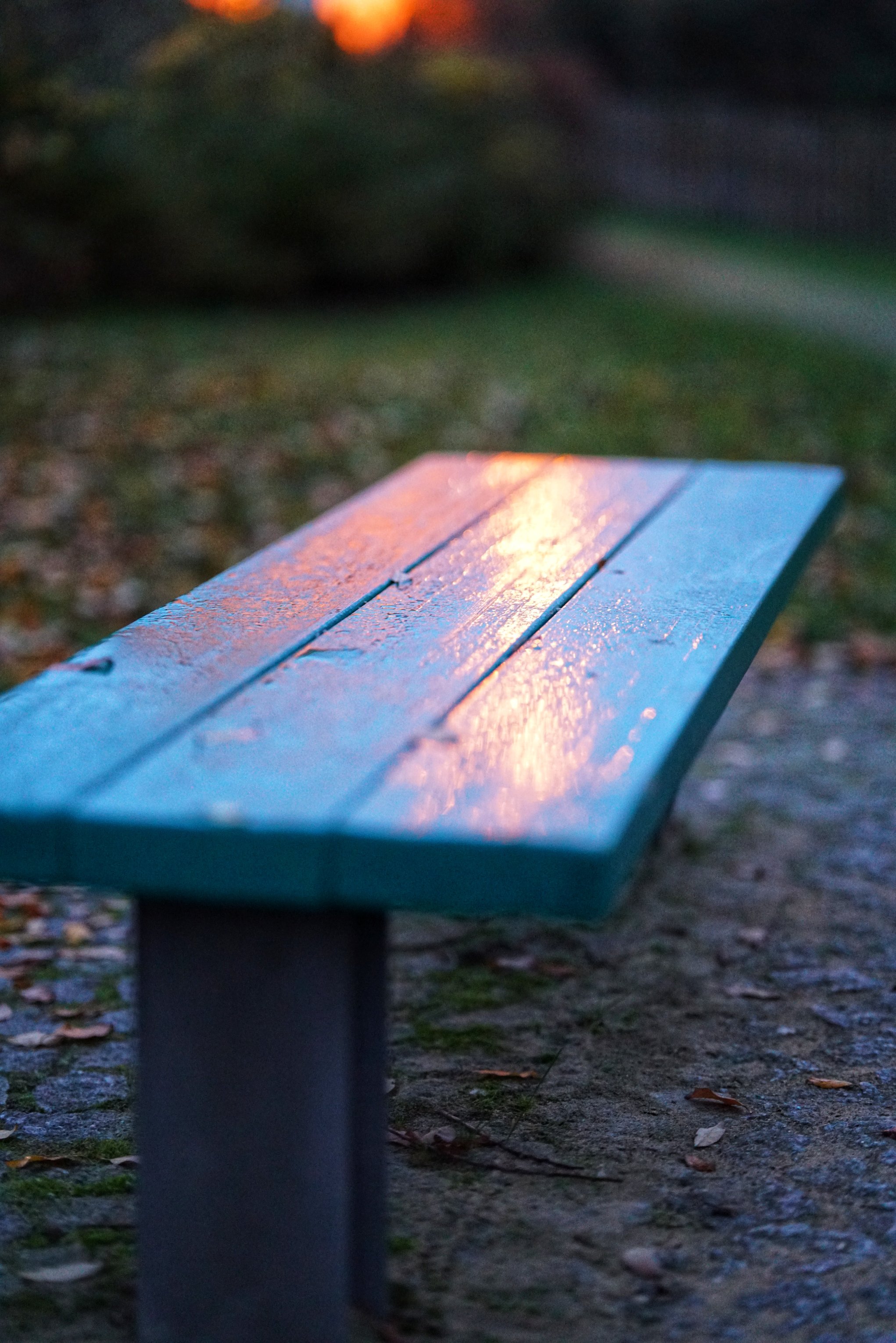 Eine feuchte Parkbank ohne Lehne, auf der sich Abendrot spiegelt 