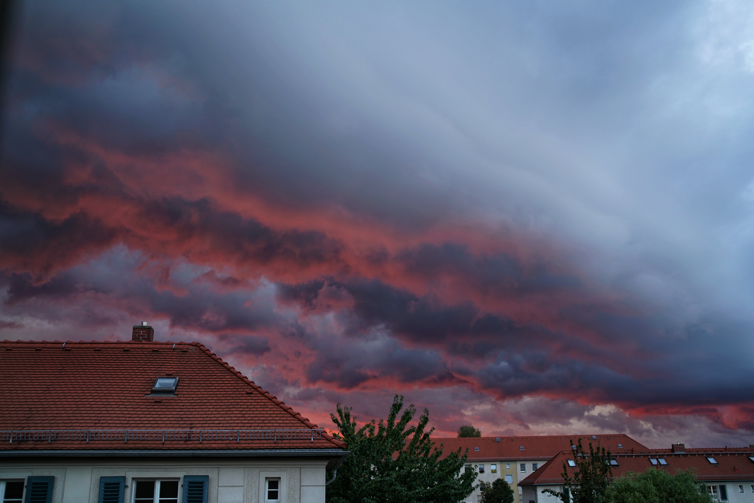 Wolken über Reihenhäusern, oben leicht hellgrau mit blau, unten grell rot bis schwarz 